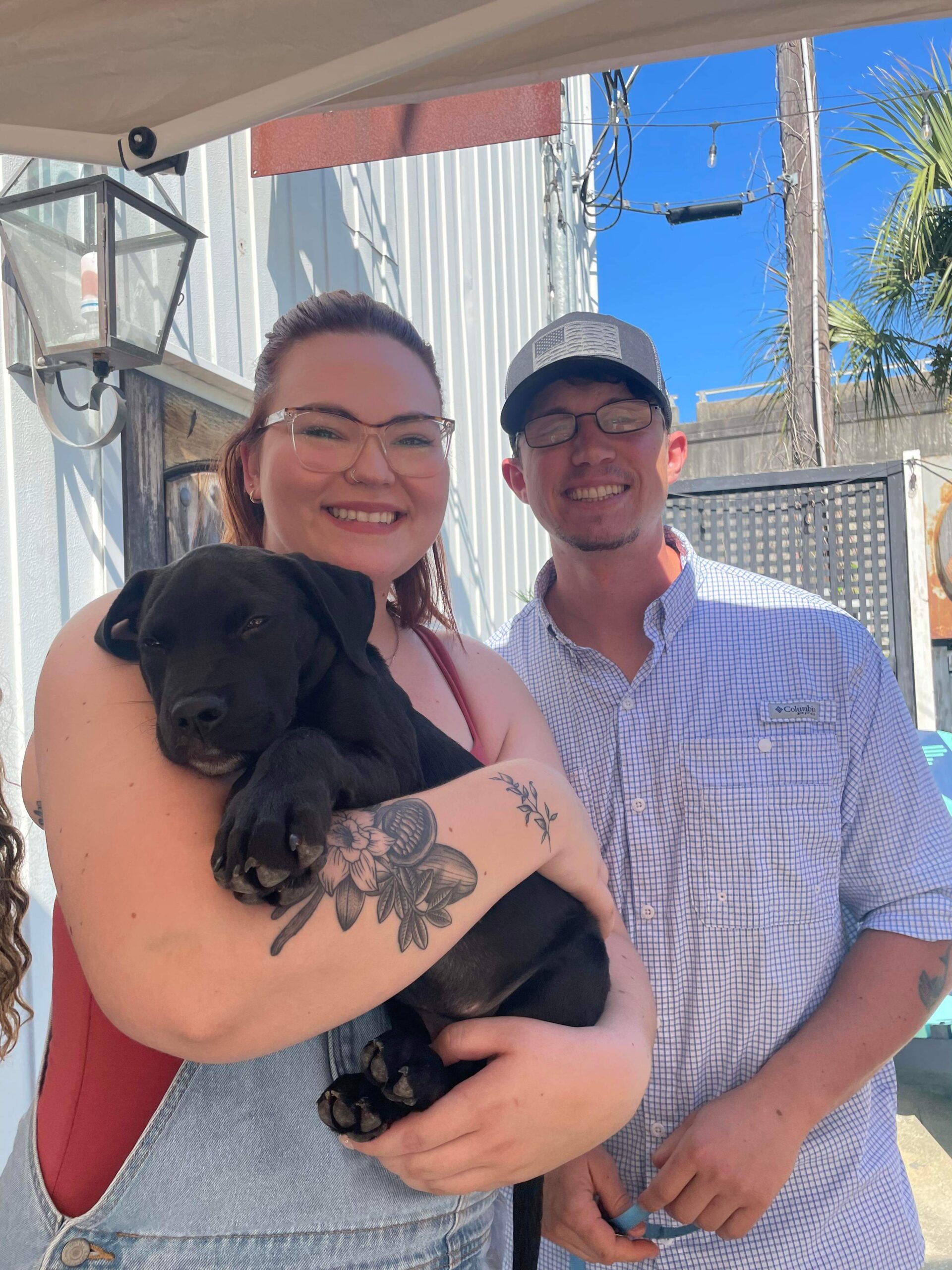 A man and a woman holding their newly adopted black puppy